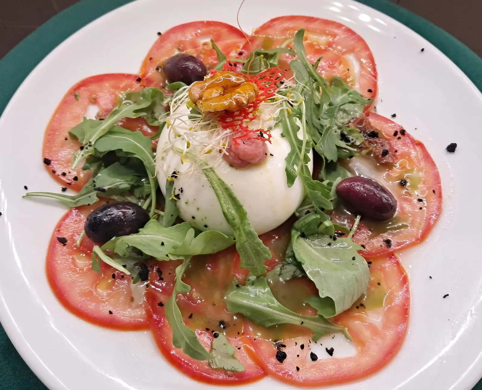 Ensalada de burrata con tomate, rúcula y aceitunas negras en plato frío del Restaurant Samuga en Sant Llorenç de la Muga, Girona