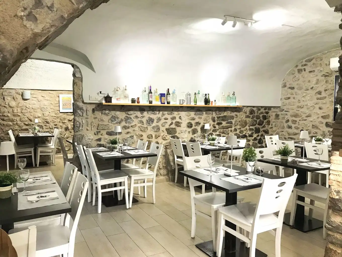 Sala interior de Restaurant Samuga en Sant Llorenç de la Muga, Girona, con bóveda de piedra, mesas montadas y sillas blancas