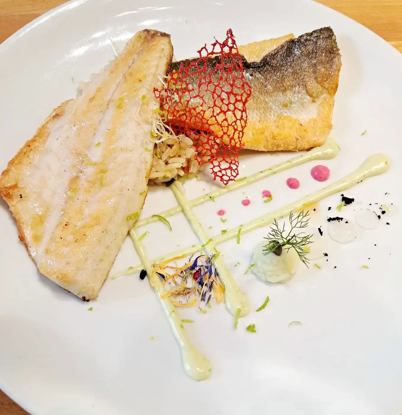 Lomo de pescado blanco a la plancha con piel crujiente, crema y brotes en un emplatado moderno en Restaurant Samuga en Sant Llorenç de la Muga, Girona