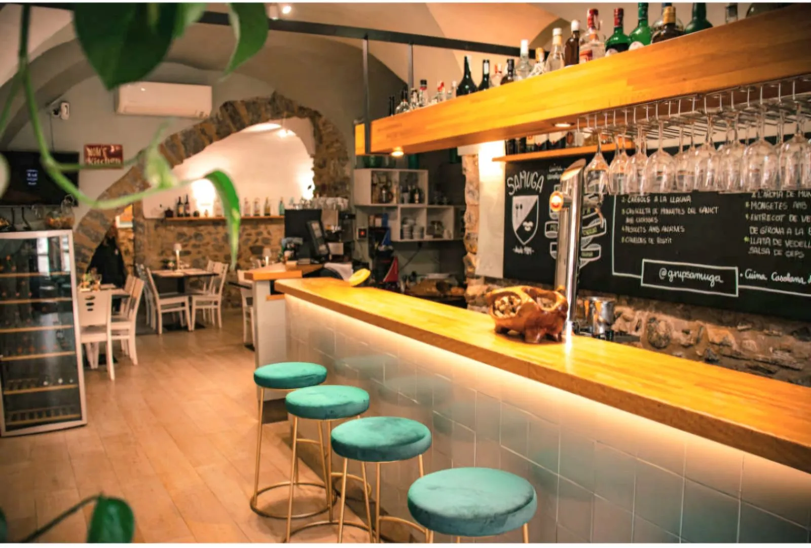 Barra de madera iluminada con taburetes turquesa en el interior del Restaurant Samuga en Sant Llorenç de la Muga, Girona