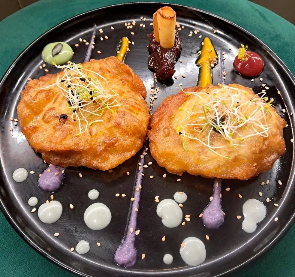 Buñuelos salados crujientes con brotes y salsas de colores en plato negro en Restaurant Samuga, cocina catalana en Sant Llorenç de la Muga, Girona