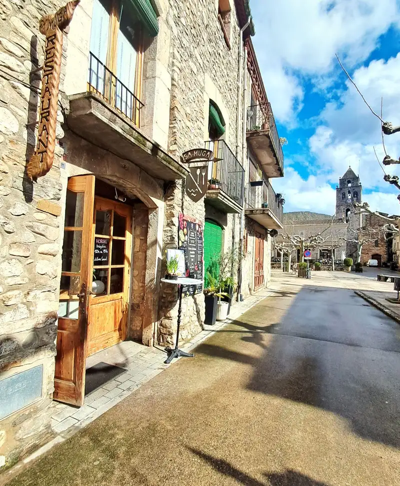 Fachada del Restaurant Samuga en Sant Llorenç de la Muga, Girona, destacando su ubicación en la plaza medieval y su cocina catalana casera.