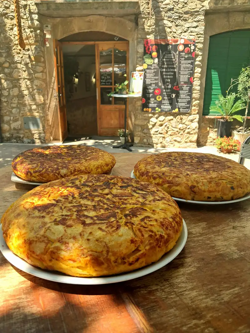Tres tortillas de patatas caseras sobre mesa de madera en la terraza del Restaurant Samuga, en la plaza medieval de Sant Llorenç de la Muga, Girona