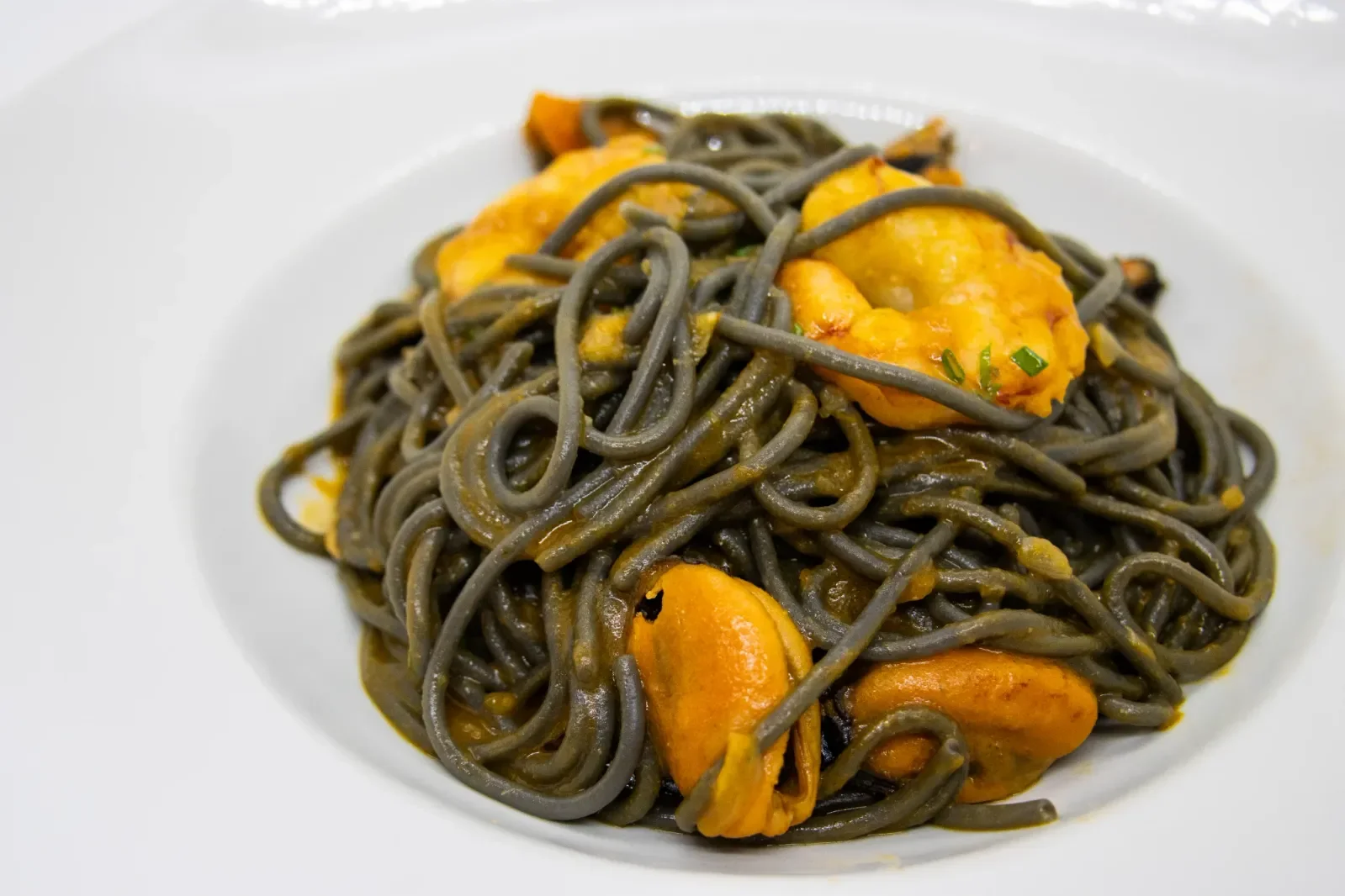 Espaguetis negros con mariscos en Agumas, restaurante de cocina mediterránea en Albanyà, Girona. Disfruta de este plato en un entorno natural excepcional.