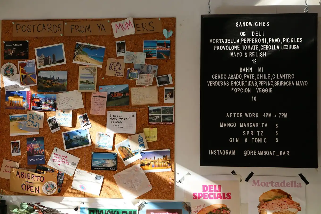 Interior del Dreamboat Bar & Deli en Sant Martí, Barcelona, mostrando una cartelera con postales y un menú de sándwiches y bebidas, ideal para afterworks.