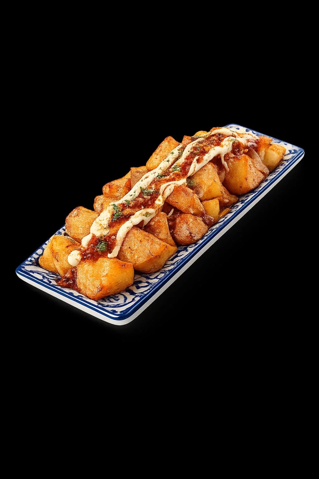 Bravas de la mama Aicha servidas en bandeja rectangular sobre fondo negro en Nomada Restaurant & Brunch, Figueres