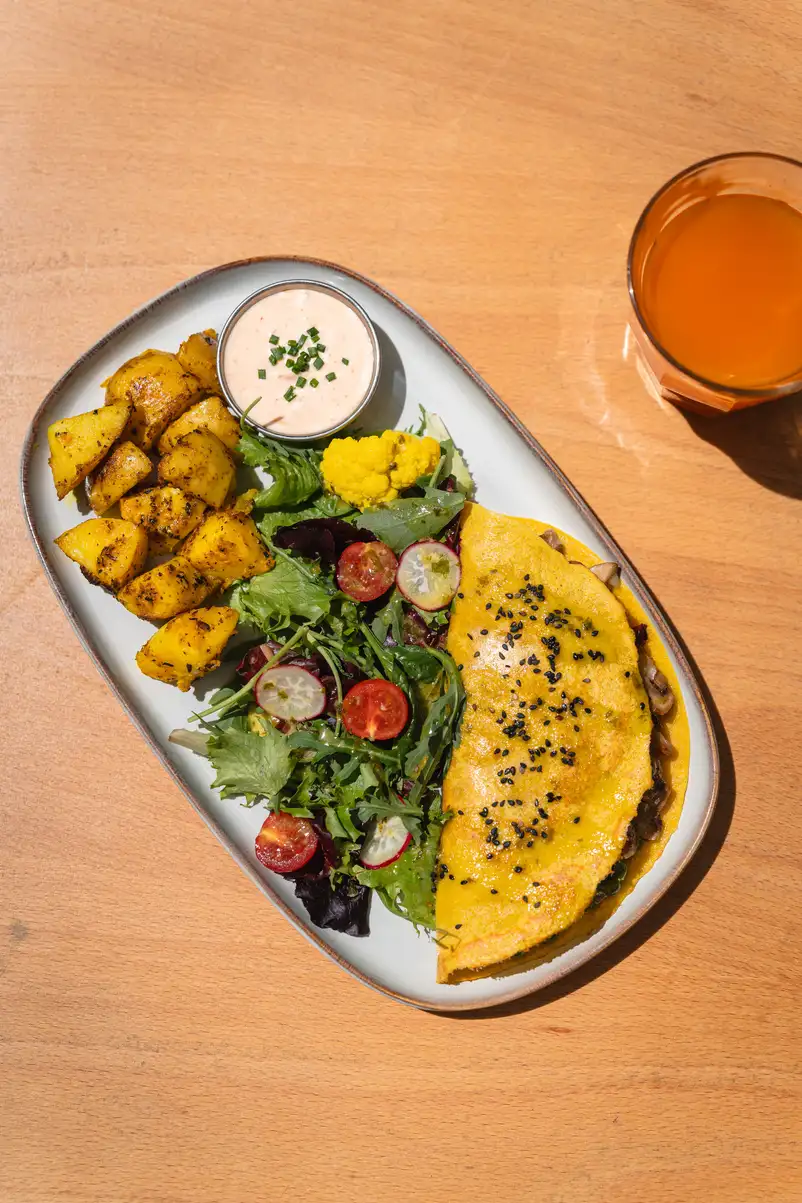 Tortilla de champiñones y queso sin gluten en Morgentau, restaurante vegano en Sant Martí, Barcelona, acompañada de ensalada y patatas.