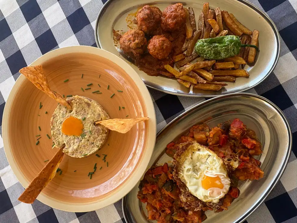 Platos del menú del día en El Pati de Vilabertran, cerca de Figueres, con huevos rotos y albóndigas con sepia, destacando su cocina variada.