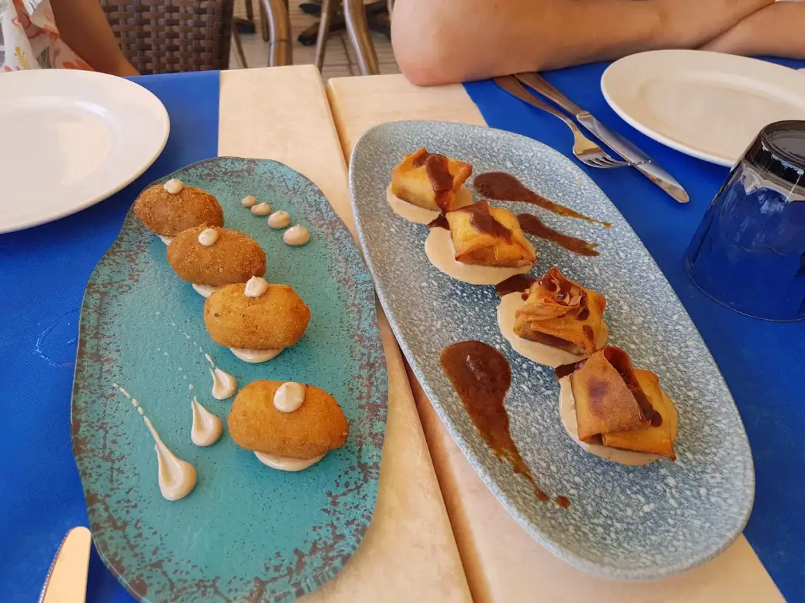 Entrantes variados en Restaurant Navili, L'Escala, con croquetas y tapas sobre platos decorativos. Cocina mediterránea frente al puerto.