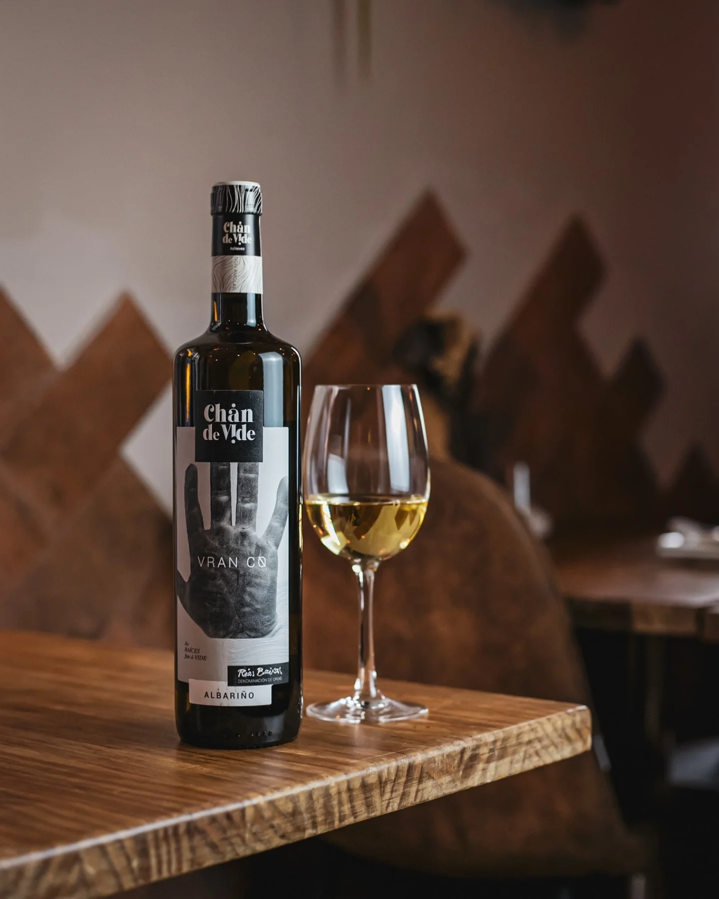 Botella de vino Albariño Chán de Vade en Amélie Restaurant, Plaça de la Vila de Gràcia, Barcelona, acompañada de una copa en una mesa de ambiente mediterráneo.