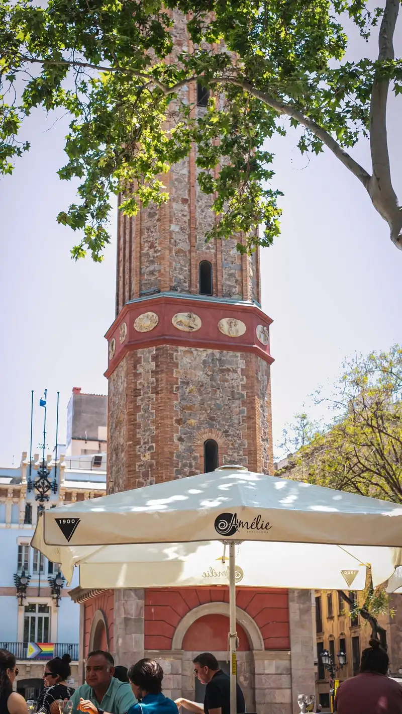 Terraza del Amélie Restaurant en Plaça de la Vila de Gràcia, Barcelona, con vistas a la torre emblemática, ideal para disfrutar de tapas de autor y cocina mediterránea.
