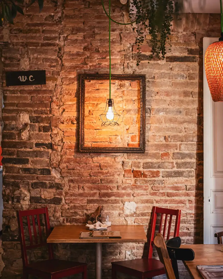 Interior acogedor de Amélie Restaurant en Plaça de la Vila de Gràcia, Barcelona, con paredes de ladrillo visto y decoración cálida.
